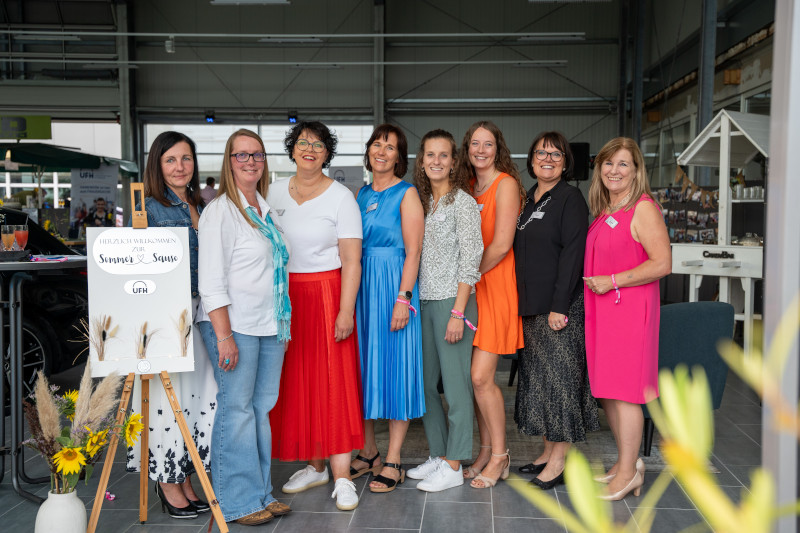 Gruppenfoto mit acht Frauen in gepflechter sommerbekleidung im Eingang einer Halle
